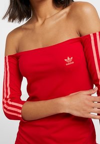 Red off-the-shoulder top with three-quarter sleeves, featuring pink stripes along the sleeves and a small Adidas logo on the chest.