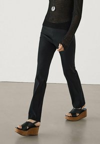 Black fitted pants with a smooth texture, paired with black wedge sandals featuring a cork platform and crisscross strap design.