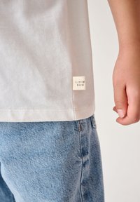 Valge puuvillane T-särk, millel on väike kangasilt "Little Bird", ja helesinised denimšortsid, millel on tekstureeritud pind.