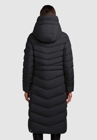 Lange zwarte pufferjas met een chevronpatroon, hoge kraag en capuchon. Beschikt over een slim fit en een textuurstof. Achteraan zijn de stiksel-details zichtbaar.