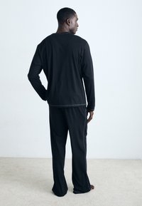 Black loungewear set featuring a long-sleeve top with a rounded neckline and loose-fitting pants. Soft texture, no visible patterns.