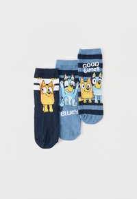 Τρία ζευγάρια μπλε ριγέ καλτσών με χαρακτήρες καρτούν σκύλων, ένα με το κείμενο "Bluey", το άλλο με το "Good times", τοποθετημένα σε λευκό φόντο.