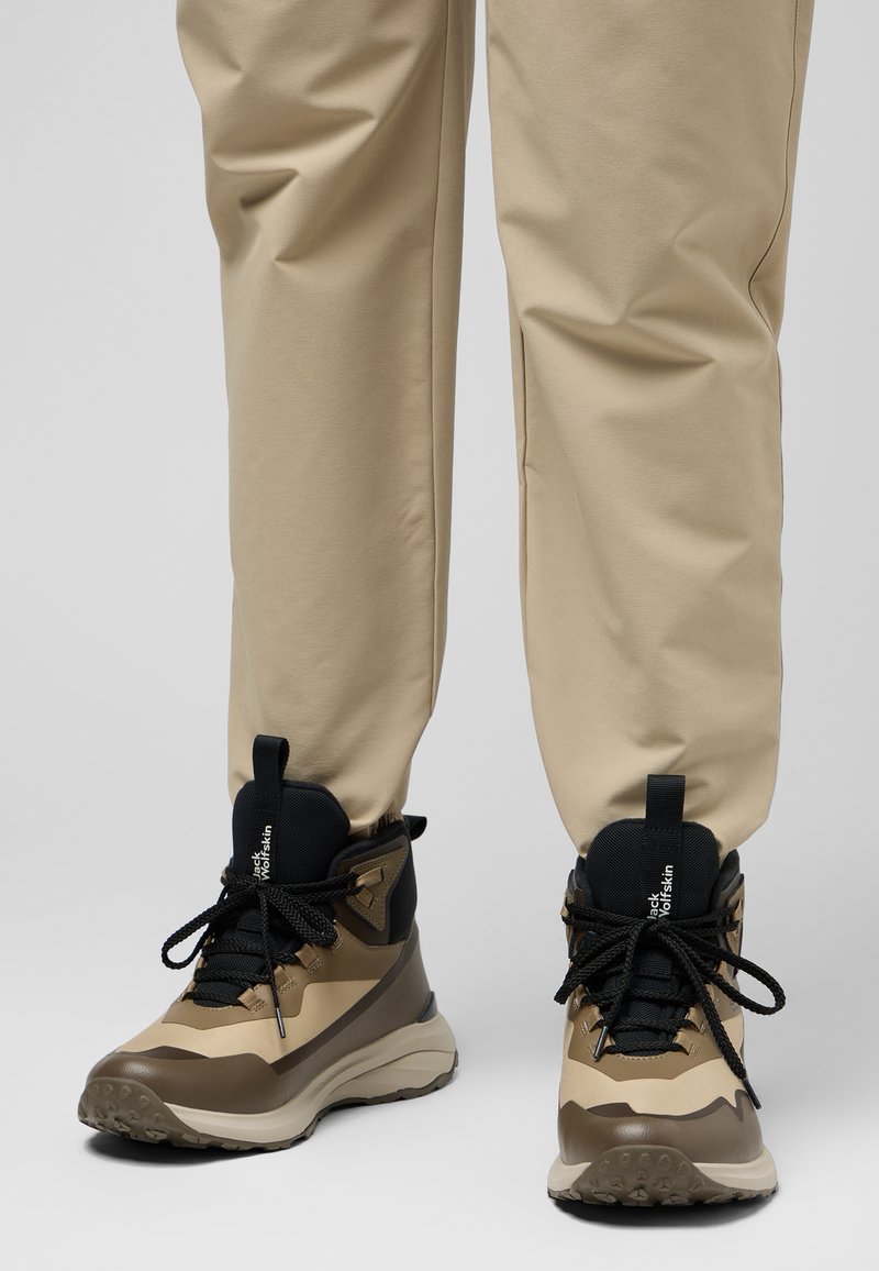 Wanderstiefel aus einer Mischung von beigem und dunkelbraunem synthetischem Material, mit schwarzen Schnürsenkeln und einer strukturierten Sohle für bessere Griffigkeit.