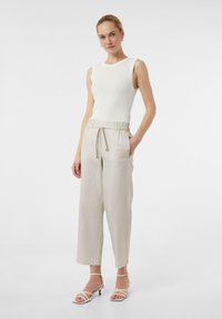 Biała, żebrowana, bezrękawnikowa bluzka zestawiona z jasnobeżowymi, luźnymi spodniami z elastycznym paskiem i sznurkiem, noszona z sandałami na paski.