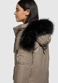 Khaki parka jope musta kunstkarusnahast kapuutsiga, tõmbluku, küljetaskute ja siledapinnalise tekstuuriga. Disainis on minimalistlik esteetika.