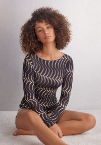Langbroekende top in donkere stof, met een golvend patroon van beige stippen, een gladde textuur en een bootnek. Aansluitend ontwerp met een glanzende afwerking.