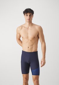 Marineblå svømmeshorts laget av stretchy stoff; har et blått stripemønster på den ene siden og en tettsittende design som slutter over kneet.