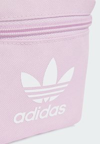 Bolsa de tela de color rosa claro con una superficie texturizada, con un logotipo de Adidas en blanco y un diseño a rayas. Incluye un cierre con cremallera.