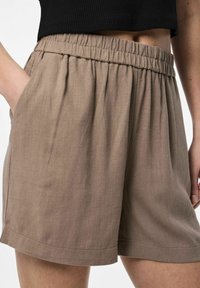 Shorts légers de couleur marron avec une taille élastique, des poches latérales et une coupe décontractée. Le tissu présente une texture subtile et une finition lisse.