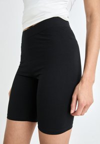 Črne raztegljive kolesarske hlače z visokim pasom, prilegajočim se dizajnom, gladko teksturo in dolžino do kolen. Brezšivna izdelava brez vidne opreme.