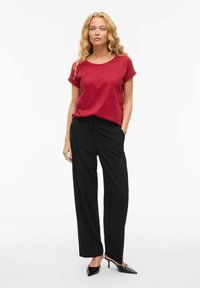 Maglietta rossa in cotone con maniche arrotolate abbinata a pantaloni neri a gamba larga. L'outfit è completato da tacchi neri appuntiti.