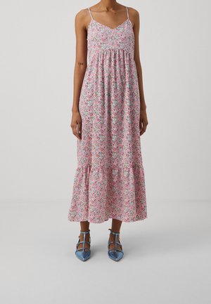Robe maxi florale rose avec des bretelles spaghetti, bustier froncé et ourlet superposé. Associée à des escarpins bleus à bout pointu.