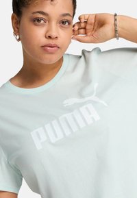 Šviesiai mėtų žalia T-marškiniai, pagaminti iš medvilnės, su dideliu baltu „PUMA“ logotipu ir apykakle. Minkšta tekstūra, laisvas siluetas.