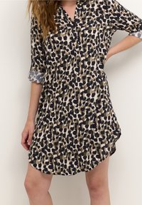 Robe à manches courtes en tissu léger, comportant un imprimé abstrait beige, noir et vert olive avec un col et des fentes latérales.