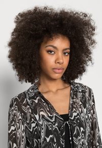Blusa transparente em preto e branco com um padrão em espiral, apresentando um fecho à frente com laço e um colarinho clássico, fabricada em tecido leve e de textura suave.