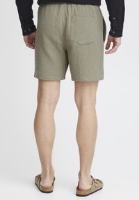 Olivengrønne bomuldsshorts med tekstureret stof, elastisk talje og baglomme. Båret med lyse sandaler.
