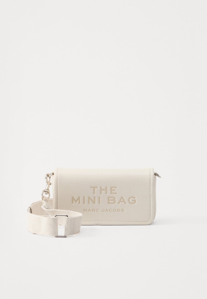 Mini bag in pelle testurizzata bianco sporco con tracolla in tessuto regolabile e testo stampato "THE MINI BAG MARC JACOBS" sul flap anteriore.
