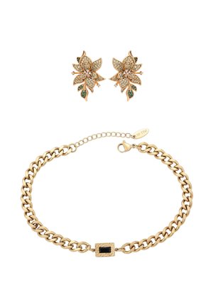 Złote kolczyki w kształcie kwiatuszków z przezroczystymi i zielonymi kamieniami, zestawione z masywną złotą bransoletką z czarnym prostokątnym zapięciem kamieniowym.