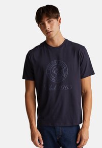 Granatowa bawełniana koszulka z krótkim rękawem z okrągłym nadrukiem logo z napisem "Colors Club" oraz "Established 1965" w kontrastującym jasnoniebieskim kolorze.