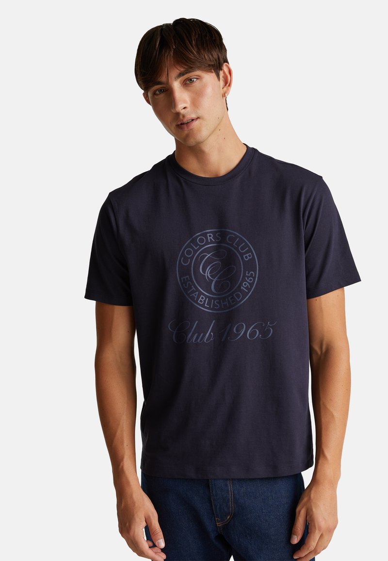 Granatowa bawełniana koszulka z krótkim rękawem z okrągłym nadrukiem logo z napisem "Colors Club" oraz "Established 1965" w kontrastującym jasnoniebieskim kolorze.