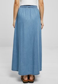 Lyseblå denim maxi skjørt med elastisk midje, flytende design og en hem som stryker gulvet, kombinert med brune sandaler.