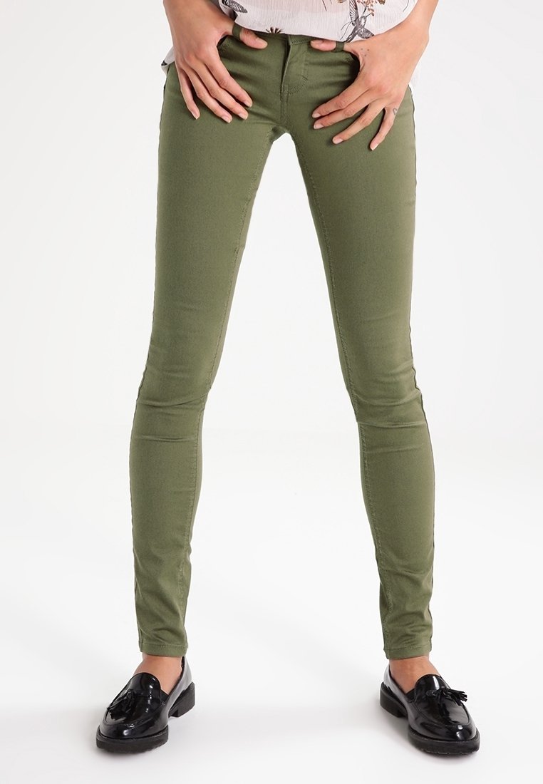 Jeans verdes oliva ajustados con una textura suave y un corte estilizado, con bolsillos estándar y terminados con mocasines negros.