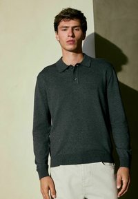 Dunkelgrauer Langarm-Polo-Pullover mit Kragen, Knopfverschluss und gerippten Bündchen, kombiniert mit hellen neutralen Hosen. Glatte Textur.