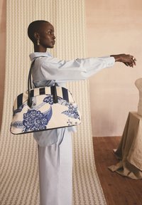 Stor strukturerad handväska i vitt canvas med marinblå blommönster, randiga detaljer och svarta läderhandtag. Mjuk textur, rundad form.