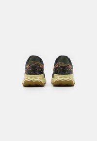 Black and olive green athletic shoes with a textured upper, speckled yellow midsole, and orange detailing on the heel and seam.