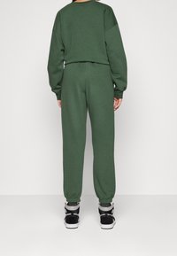 Grön bomullströja och byxset, med en avslappnad passform, ribbade ärmslut och en mjuk yta. Bärs tillsammans med svarta högskor.