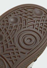 Sola de sapato de borracha na cor castanha, com padrões texturizados que incluem grelhas, círculos e saliências para maior aderência.