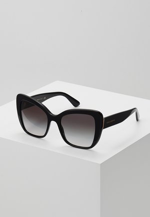 Lunettes de soleil oversize noires avec des verres gris dégradés, monture en plastique lisse et accents en métal doré sur les branches.