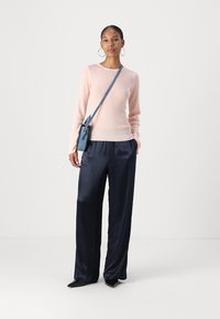 Maglione a coste rosa chiaro con maniche lunghe, abbinato a pantaloni palazzo in satin blu navy. Il modello porta una piccola borsa a tracolla blu.