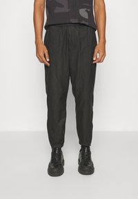 Černé tapered tepláky s elastickým pasem, hladkým povrchem a žebrovanými manžetami, doplněné černými šněrovacími teniskami.