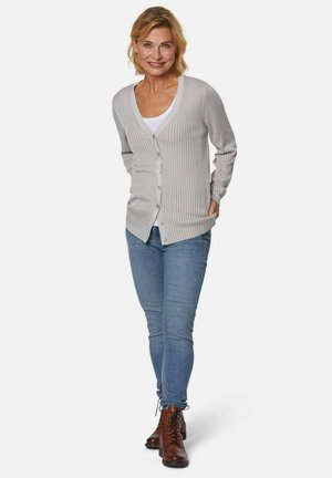 Lichtgrijze geribbelde cardigan met een V-hals, knoopsluiting en lange mouwen, gecombineerd met blauwe skinny jeans en bruine veterschoenen.