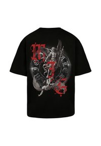 Μαύρο βαμβακερό t-shirt με λεπτομερή γραφική εκτύπωση φτερωτών φιγούρων και κόκκινες επιγραφές στην πλάτη, που παρουσιάζει πολύπλοκα σχέδια και υφές.