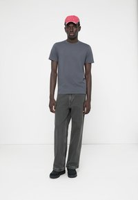 Tricou gri, blugi negri lejeri și pantofi negri. Șapcă roz cu un design brodat. Un aspect simplu, casual, cu culori solide în întreaga ținută.