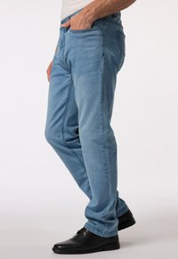 Světle modré džíny s rovnými nohavicemi, předními kapsami a viditelným pasem; v kombinaci s černými botami.