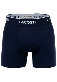 Granatowe bawełniane szorty baweliane z białą elastyczną taśmą w pasie, oznaczoną napisem „LACOSTE”. Charakteryzują się dopasowanym krojem i bezszwowymi nogawkami dla wygody.