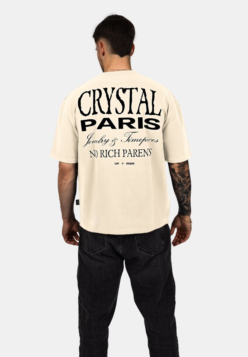 Krémové oversized tričko s výrazným černým textem: "CRYSTAL PARIS Šperky a Hodinky BEZ BOHATÝCH RODIČŮ" na zádech.