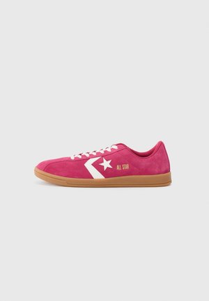 Niski różowy zamszowy sneaker z białym logo gwiazdy w jodełkę, białymi sznurowadłami, "All Star" złotym napisem i gumową podeszwą na jednolitym tle.