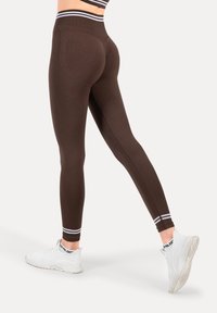 Brązowe legginsy z wysokim stanem i białymi paskami przy kostkach. Wykonane z elastycznego materiału, o dopasowanym fasonie i bez widocznych szwów.
