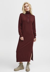 Mörkröd långärmad klänning med halvdragkedja vid kragen, sidoslits och ribbade ärmslut, bärs med beige snörda kängor. Mjuk stickad textur.