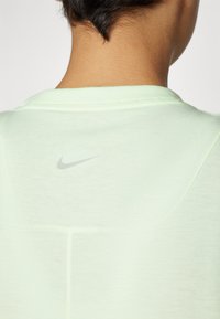 Lys grønn Nike skjorte med rund halslinning og en liten, reflekterende logo plassert på baksiden. Har et mykt, teksturert stoff.