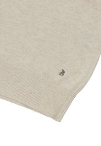 Beżowy sweter dzianinowy z ribbowym dołem i subtelną teksturą. Zawiera mały, metaliczny akcent z logo w pobliżu krawędzi.