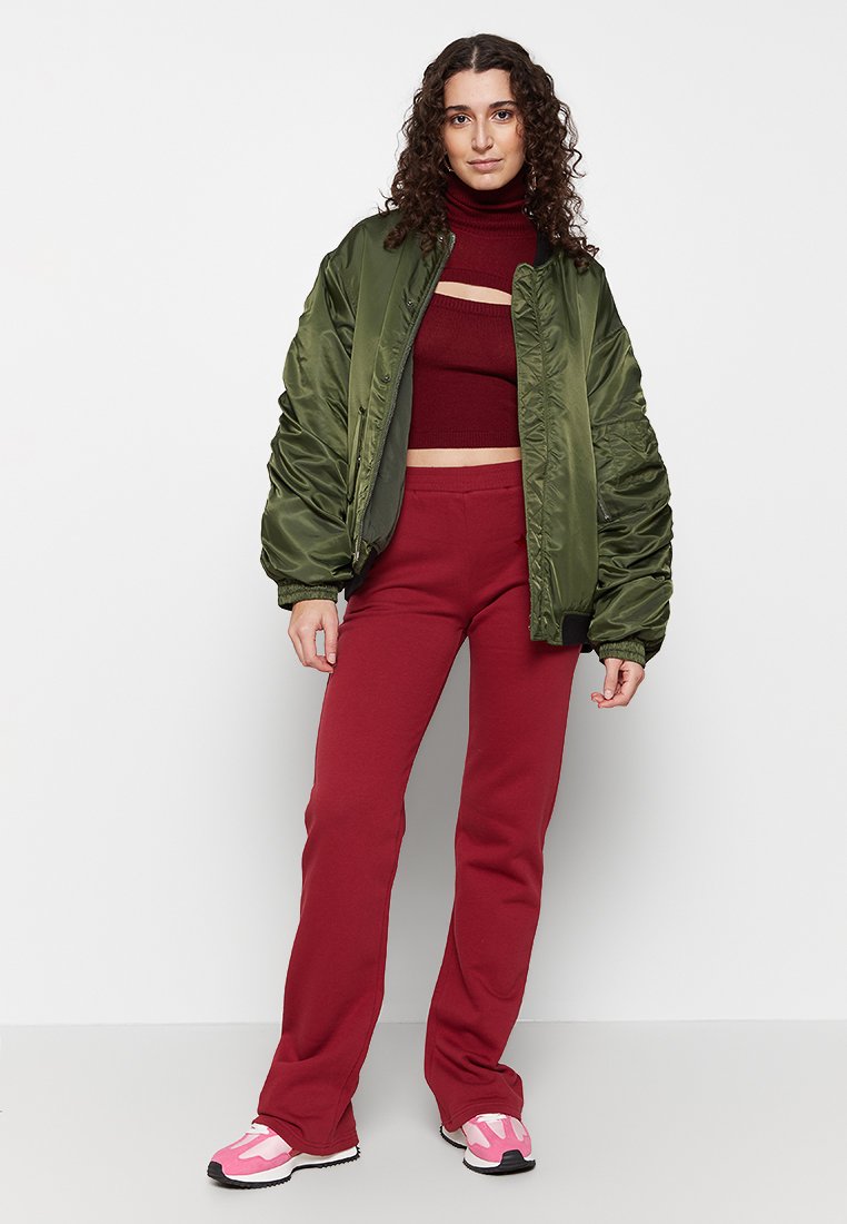Olivegrüner, gepolsterter Bomberjacke, burgunderfarbenem Cropped-Sweater, roten Schlaghosen und rosa Sneakers mit schwarzen Sohlen. Sanfte Texturen überall.