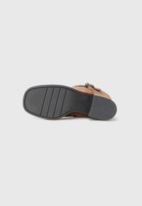 Bruine leren schoen met een gestructureerde zool, met een beslagdetail en een gladde afwerking op de bovenkant. Gevoerde binnenzool voor comfort.