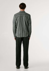 Camicia a maniche lunghe, con colletto, a scacchi in tonalità di verde e grigio, con orlo dritto; abbinata a pantaloni scuri a gamba dritta.