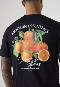 Czarna koszulka z kolorową grafiką pomarańczy i liści na plecach, z napisem "MODERN ESSENTIALS" i "Closure London Studios".