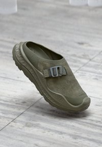 Λαδί ελαστικό παπούτσι με σουέτ επάνω μέρος, καουτσούκ σόλα και μεταλλική λουρίδα για ασφαλή εφαρμογή. Ορατή υφή και καμπύλες.